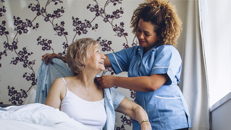 Care worker helping a woman put her shirt on