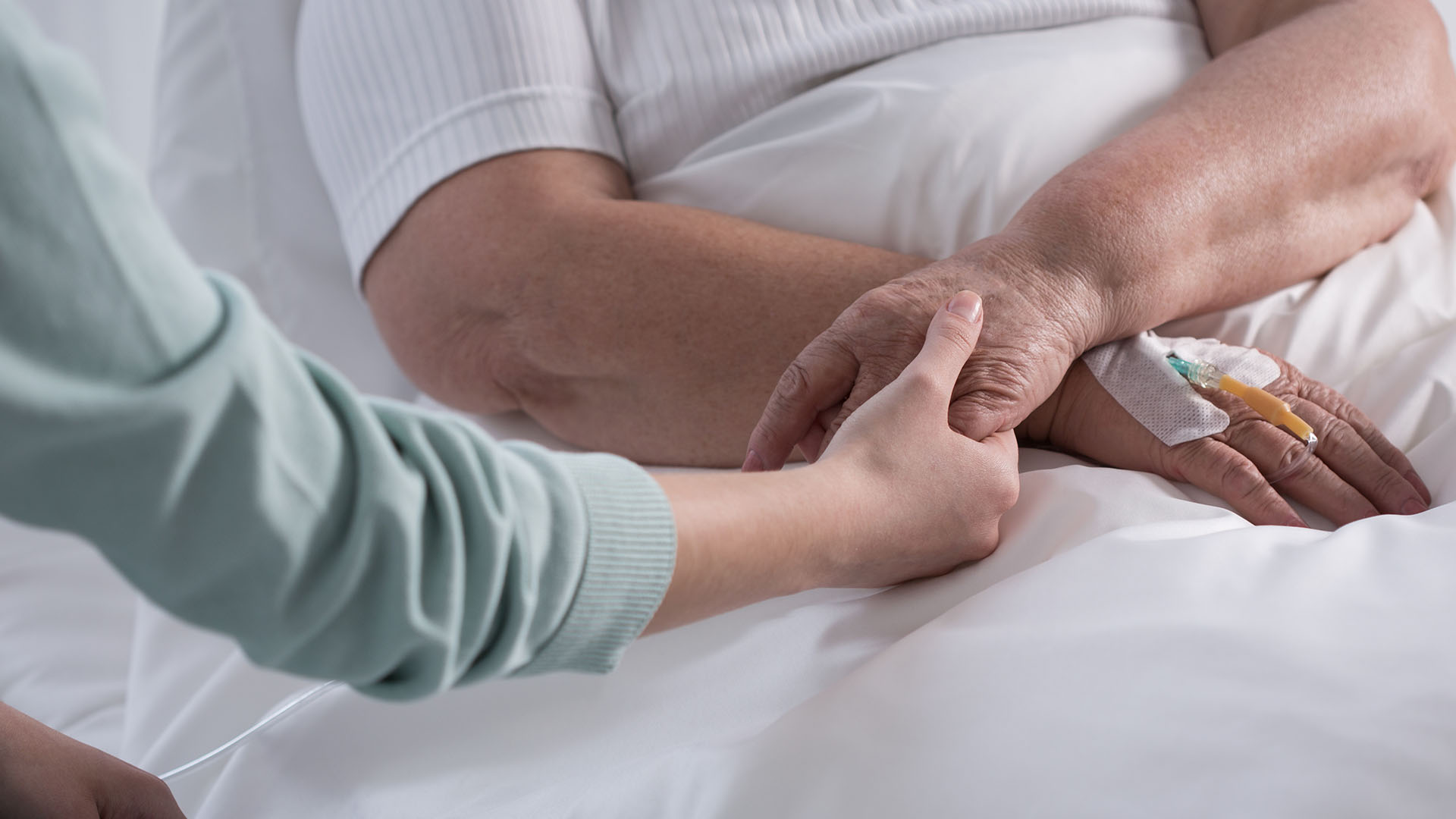 Someone holding hands with a person with a canula in a hospital bed.