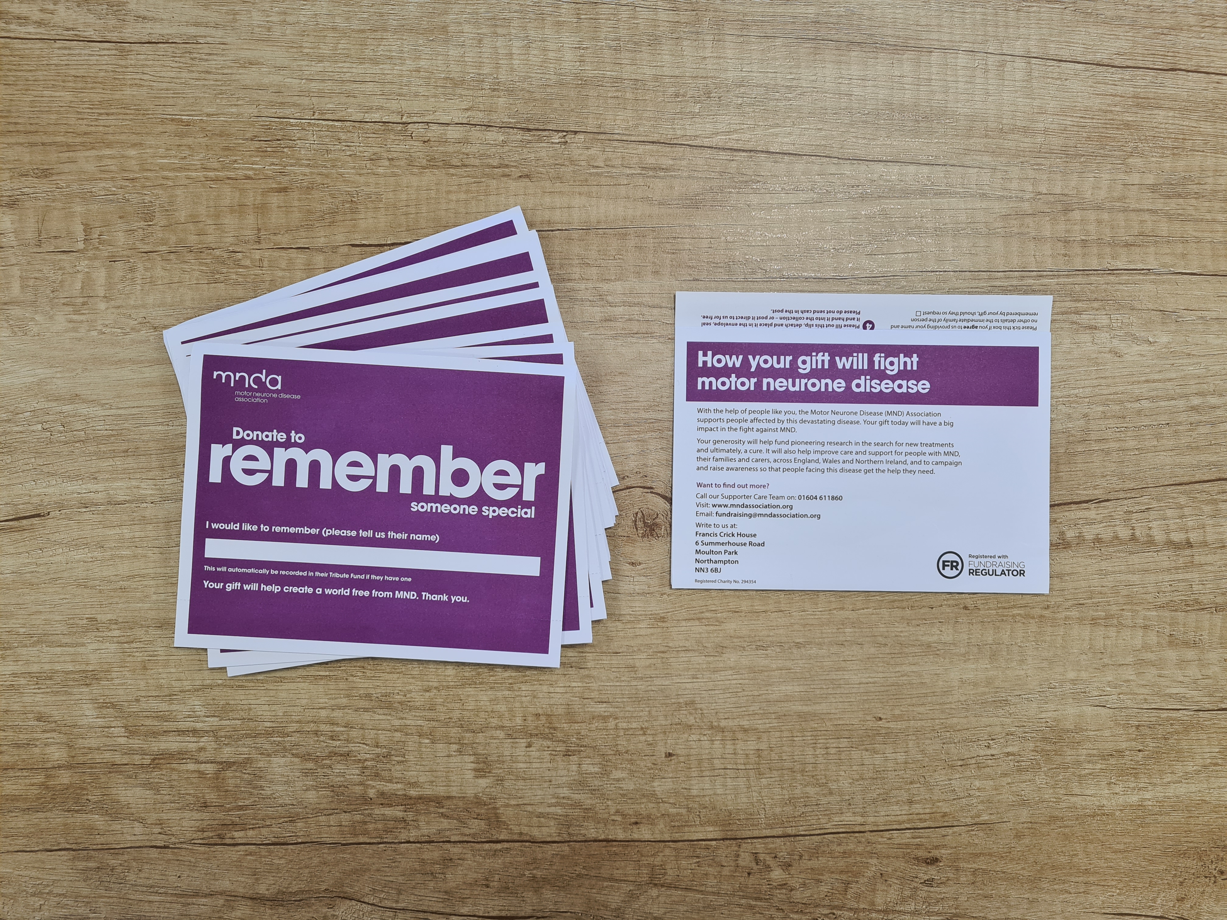 Purple collection envelopes fanned out on the left of a wooden table with reverse of one envelope on the right of the wooden table 