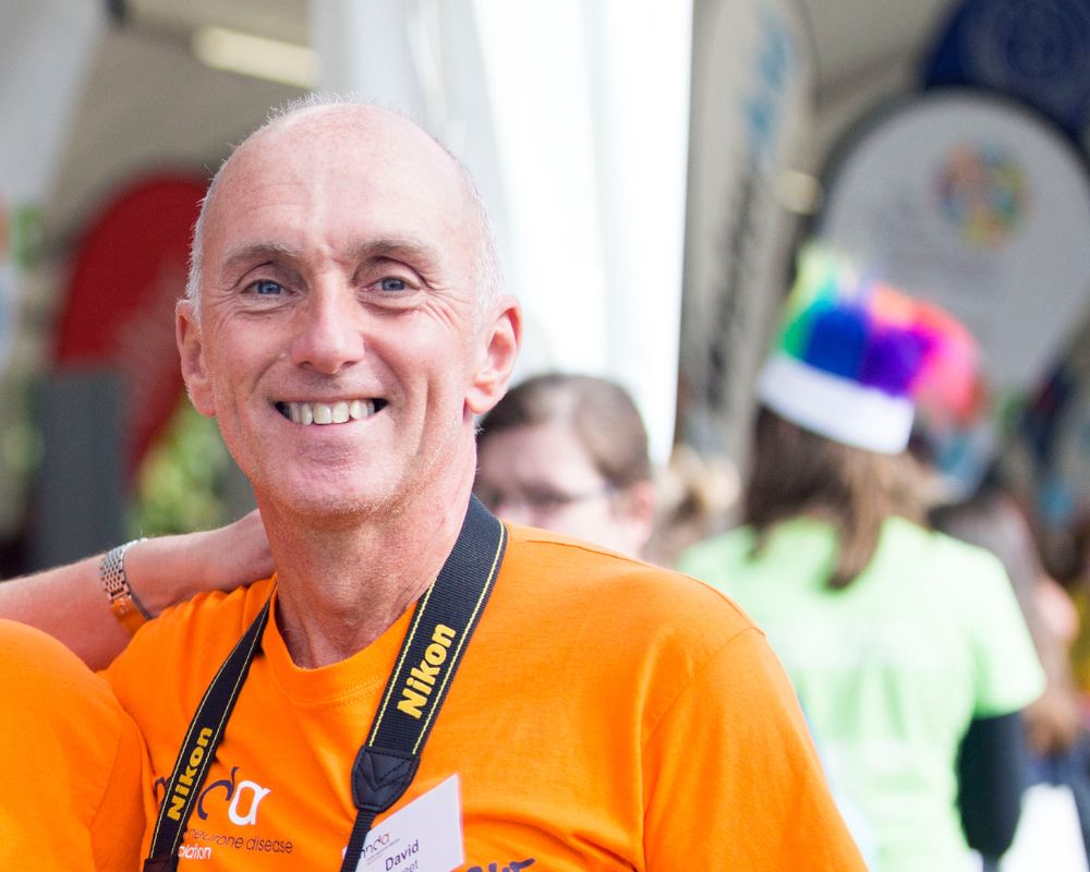 Supporter David Sweet looking directly at camera wearing orange MND Association T shirt at a running event