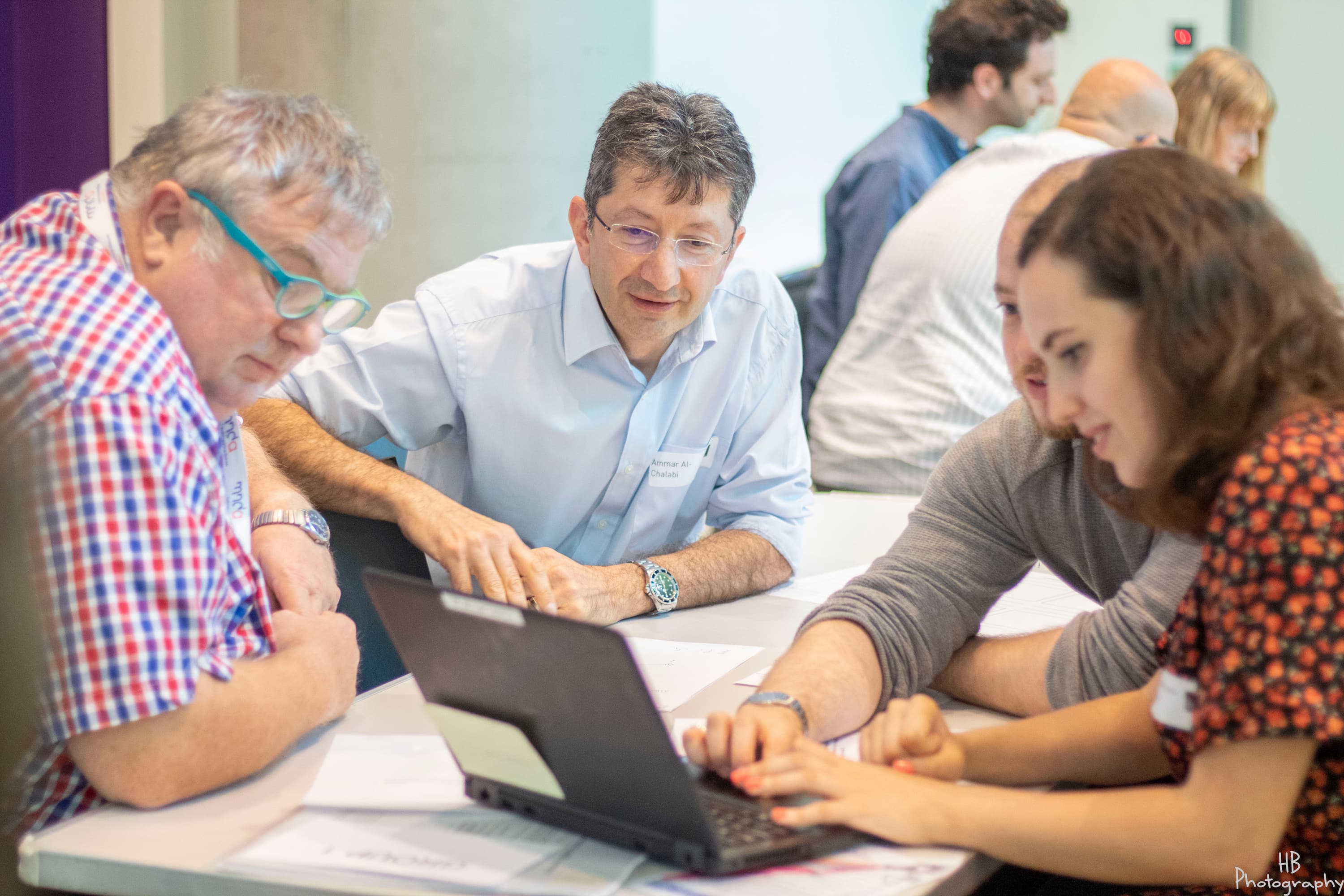 A group of people sitting around a table, looking at a laptop