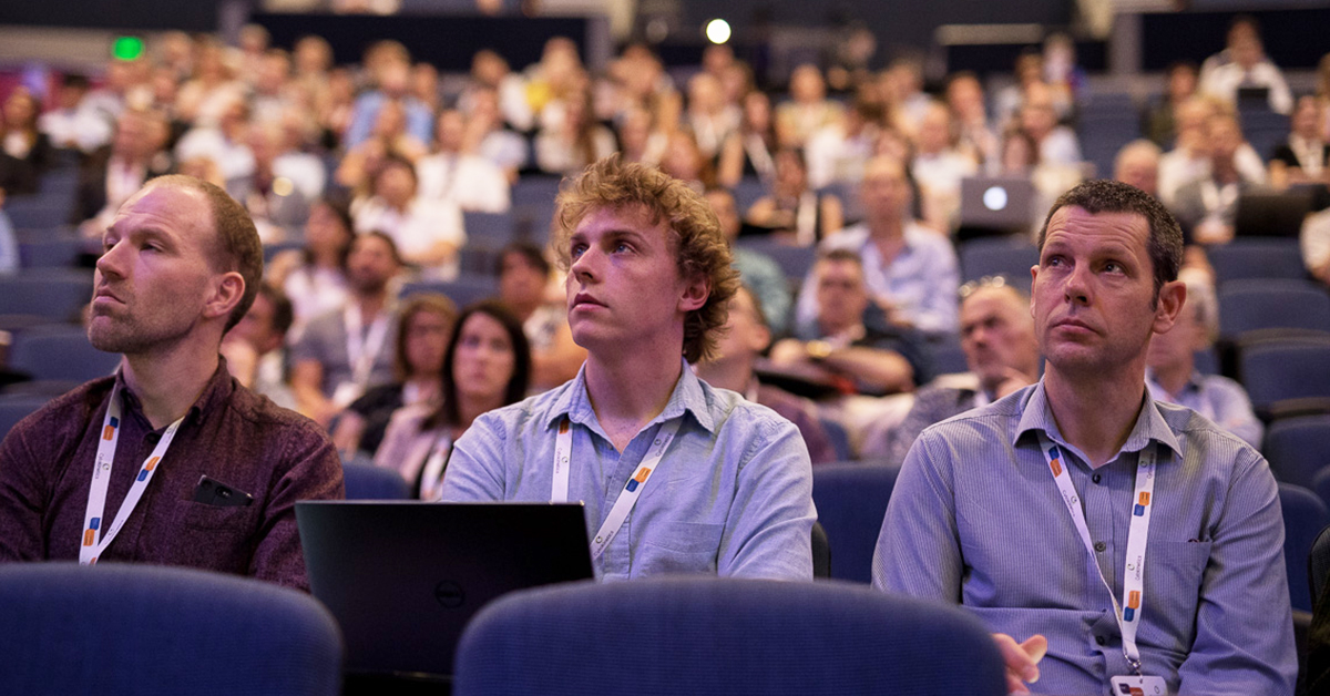Nick with fellow researchers, listening to a talk in a lecture hall.
