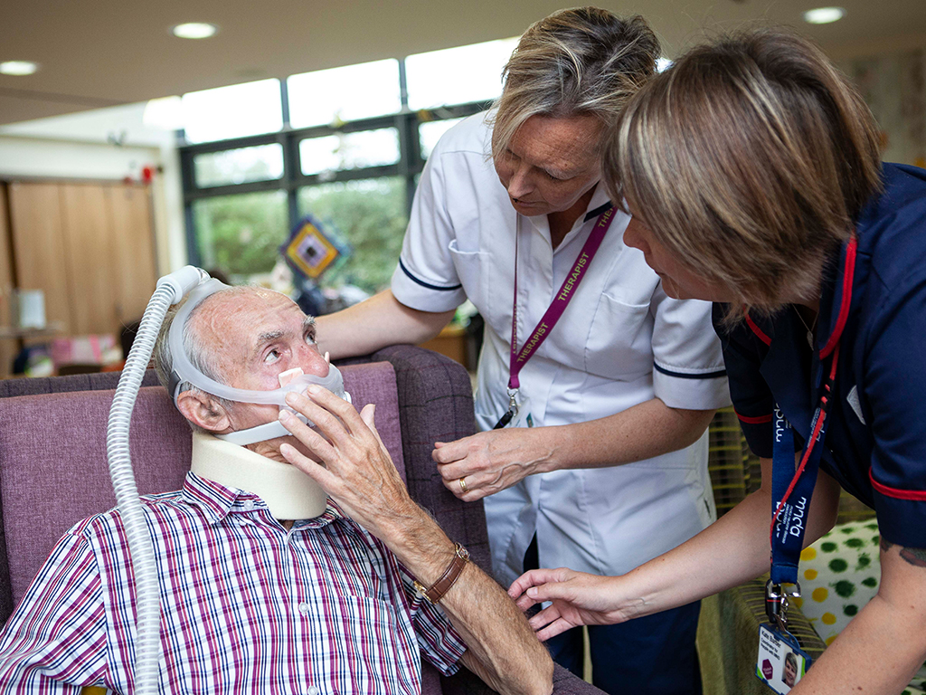 Two professionals assisting a man wearing an NIV mask