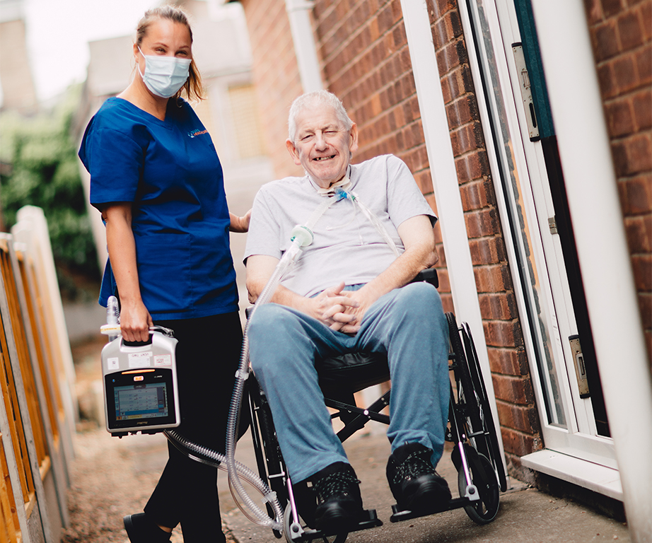 healthacre professional and person in wheelchair outside family home with medical equipment 