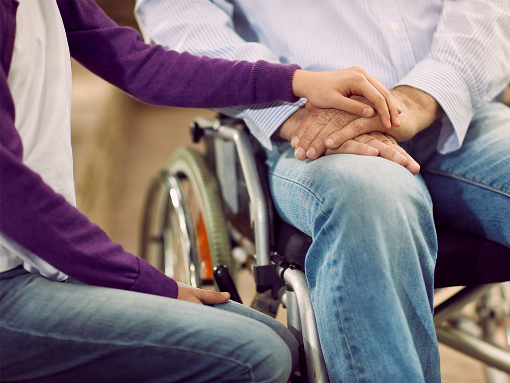 person in wheelchair holding hands of younger person 