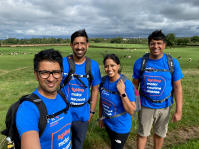 Four people wearing MND Associaition t-shirts walking in the middle of a field.