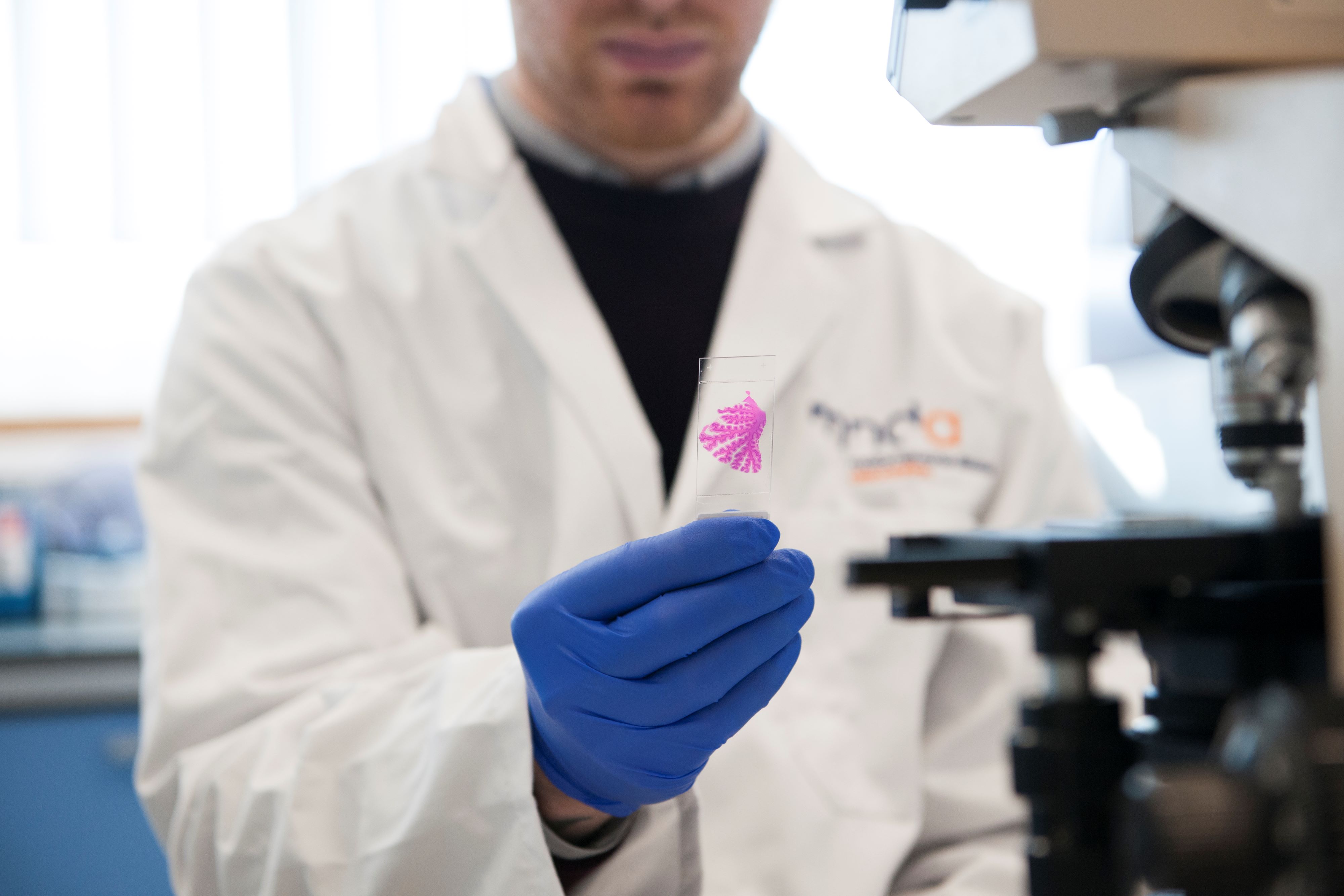 A photo of a researcher in a MND Association lab coat with a microscope