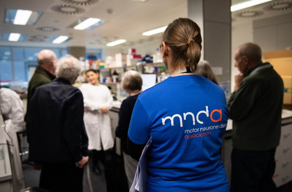 Picture of people take laboratory tour. Image focuses on person in forefront of photo wearing blue MND Association t-shirt