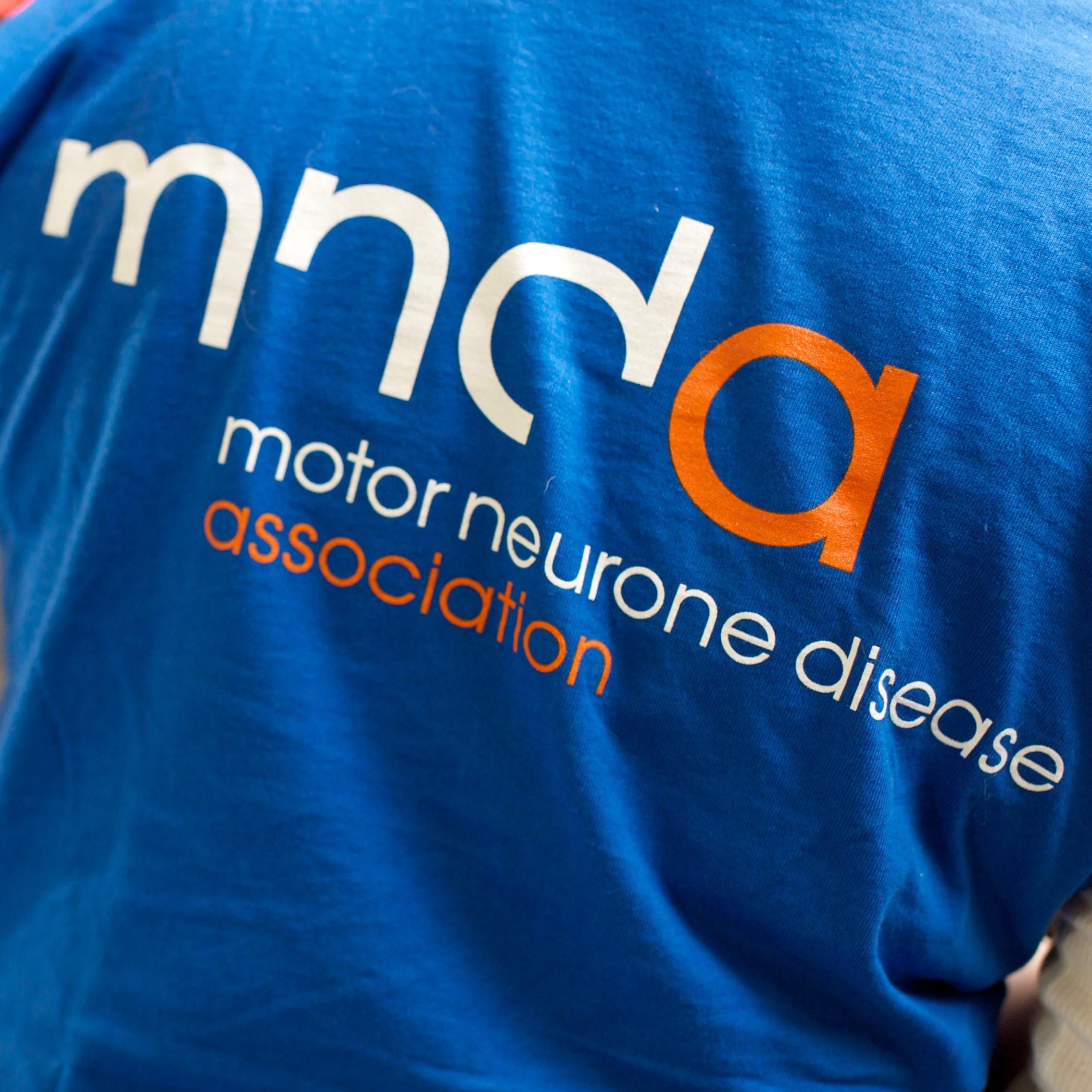 The back of a blue MND Association t-shirt, featuring our logo. The person is at an event.