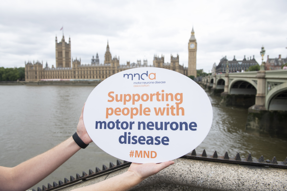 A picture of an MND Association volunteer holding a "Supporting people with Motor Neurone Disease" sign outside Parliament..