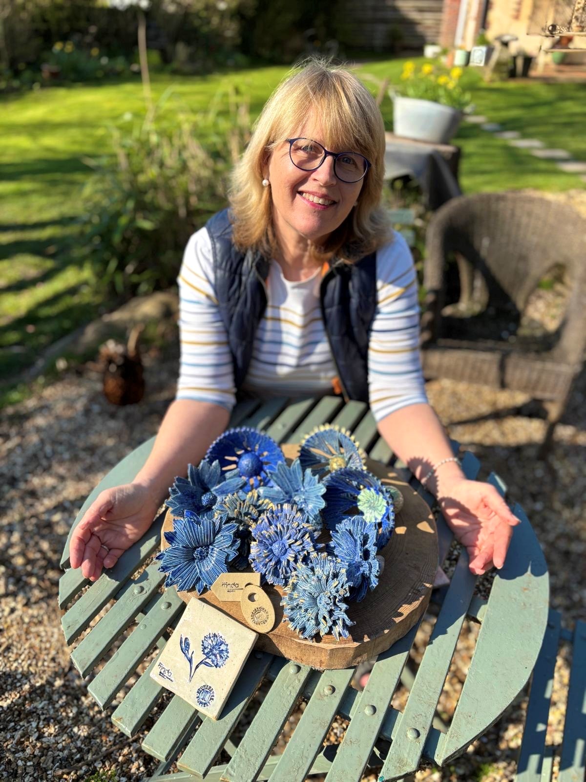 Linda sits in the garden showing the blue cornflowers made for fundraising