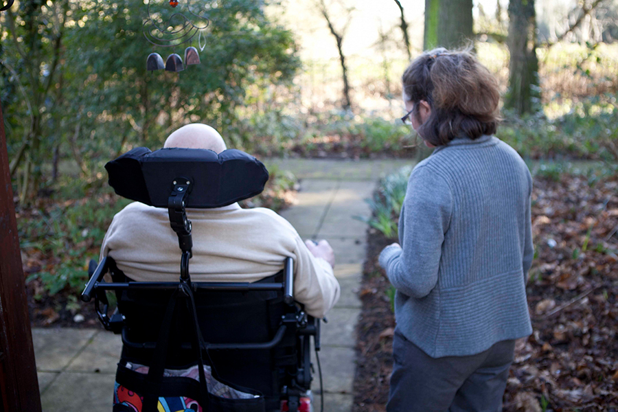 A woman walking alongside a man in a wheelchair in a hospice garden.