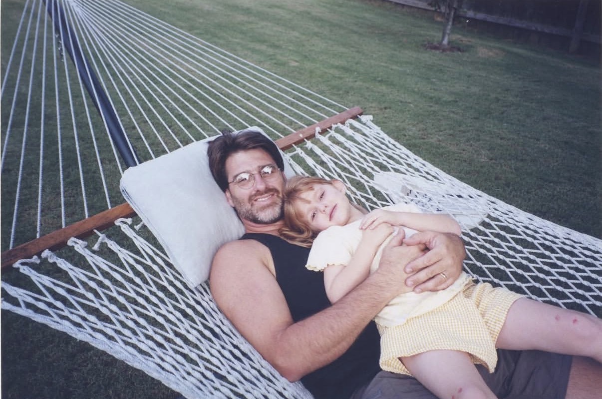 Amelia with her dad when she was young. They lay on a hammock smiling to camera. 