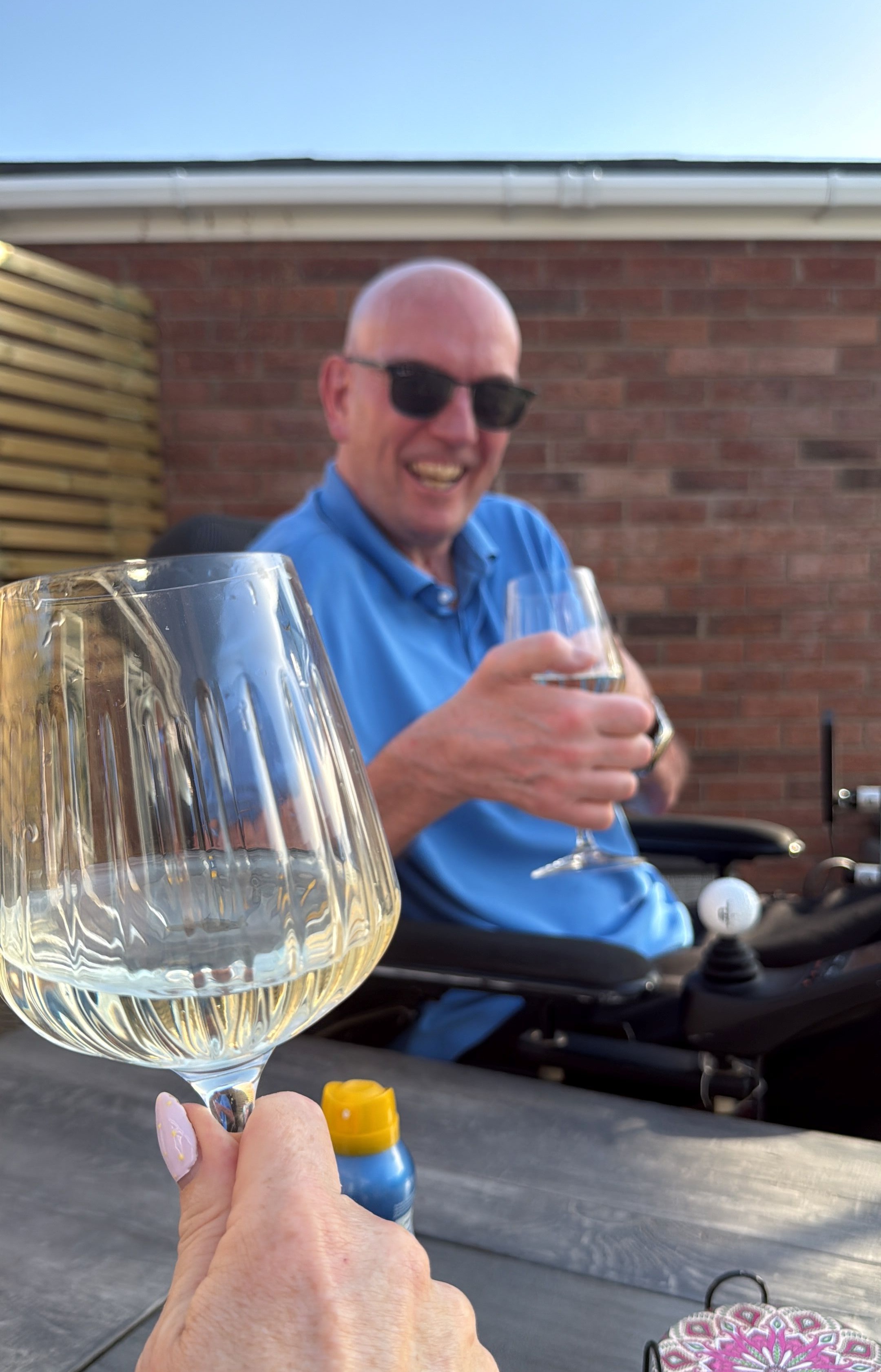 Keith smiling in the garden enjoying a glass of white wine