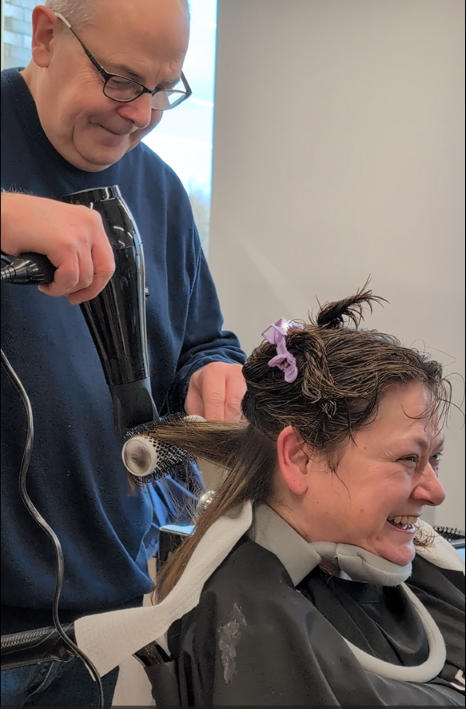 Matt blow drying Gill's hair. She watches him in the mirror, smiling.