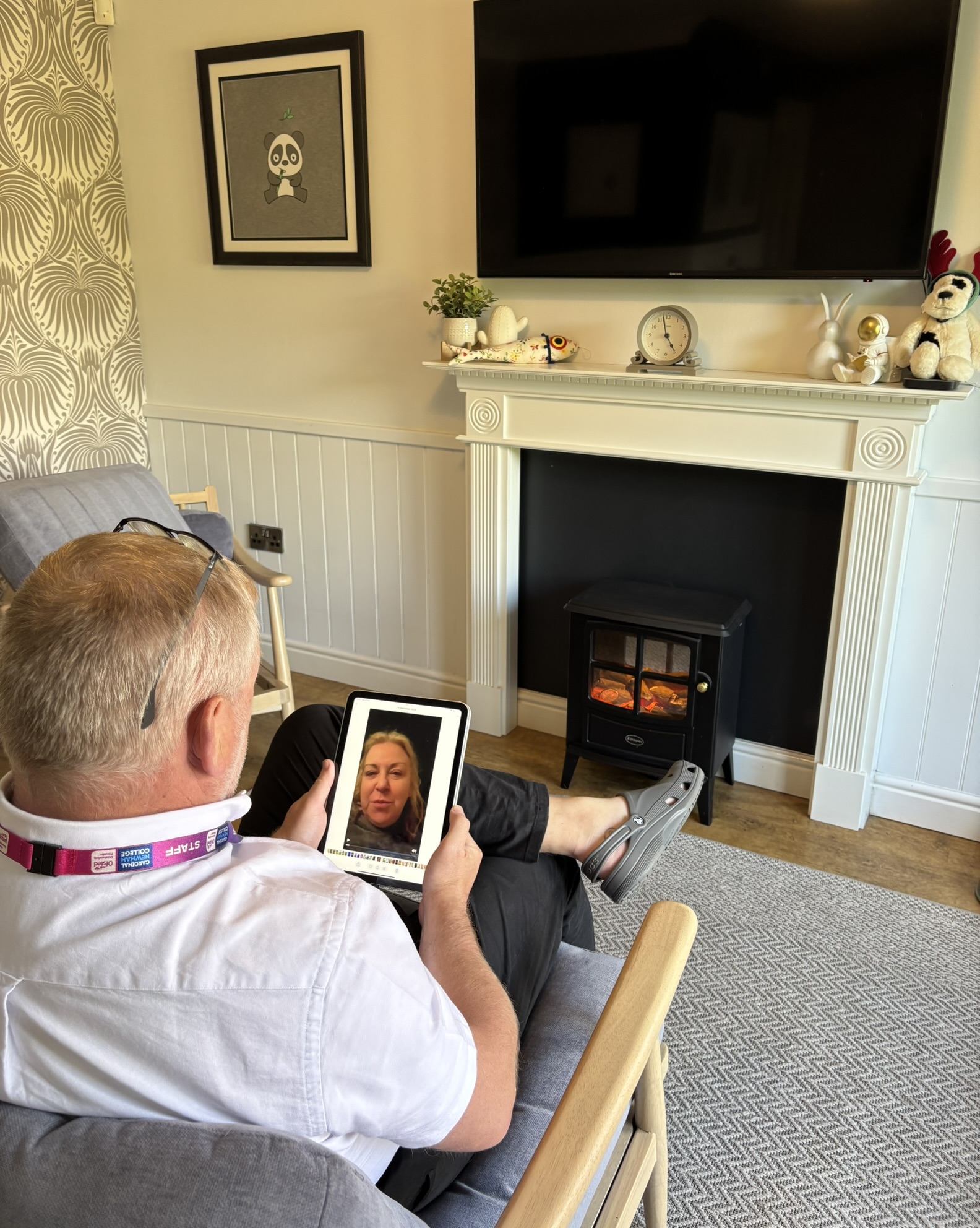 John watches the video Julie left. He sits on a chair in their living room, watching on a tablet.