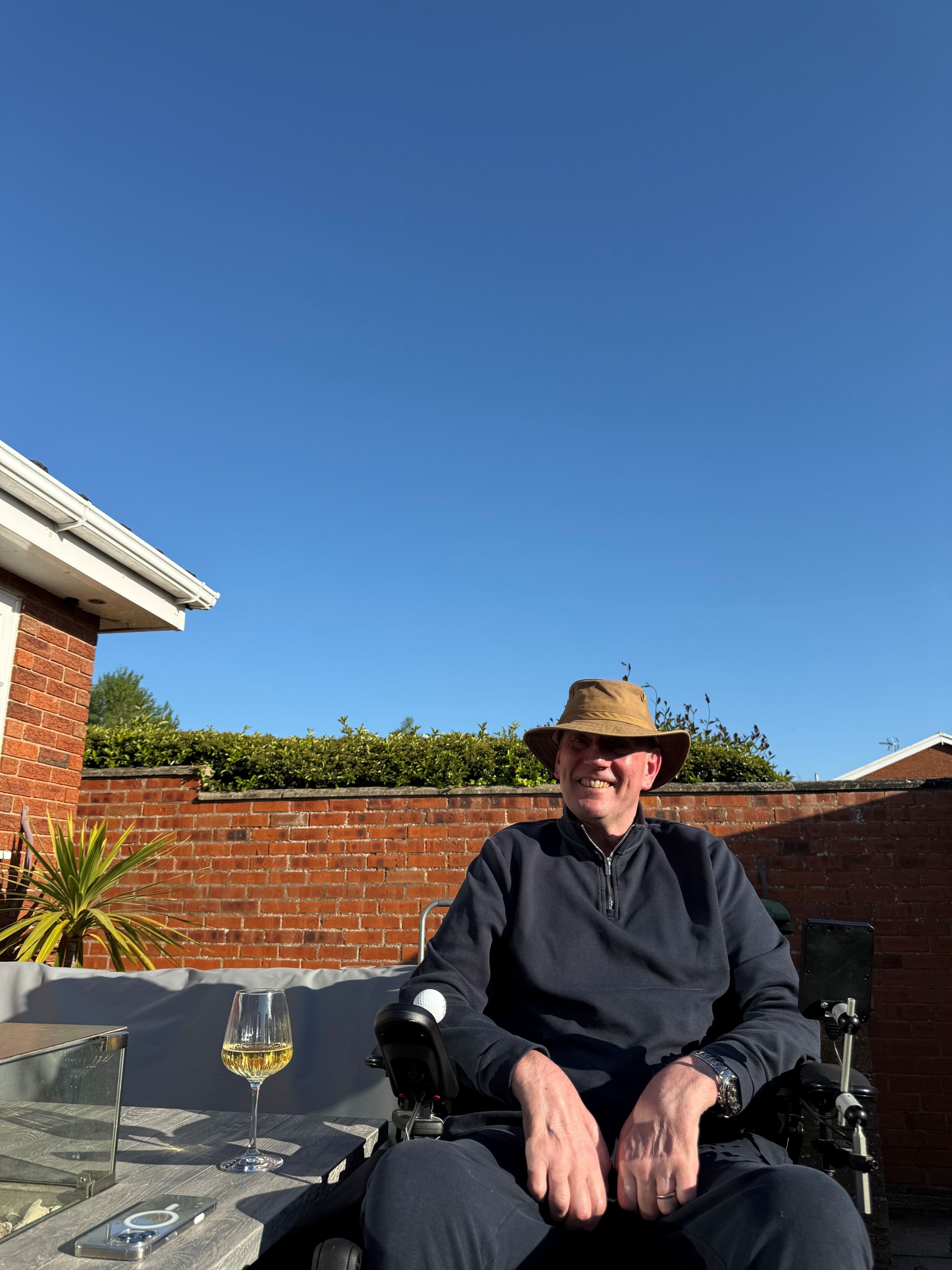 Keith in the garden with a glass of white wine, smiling to camera