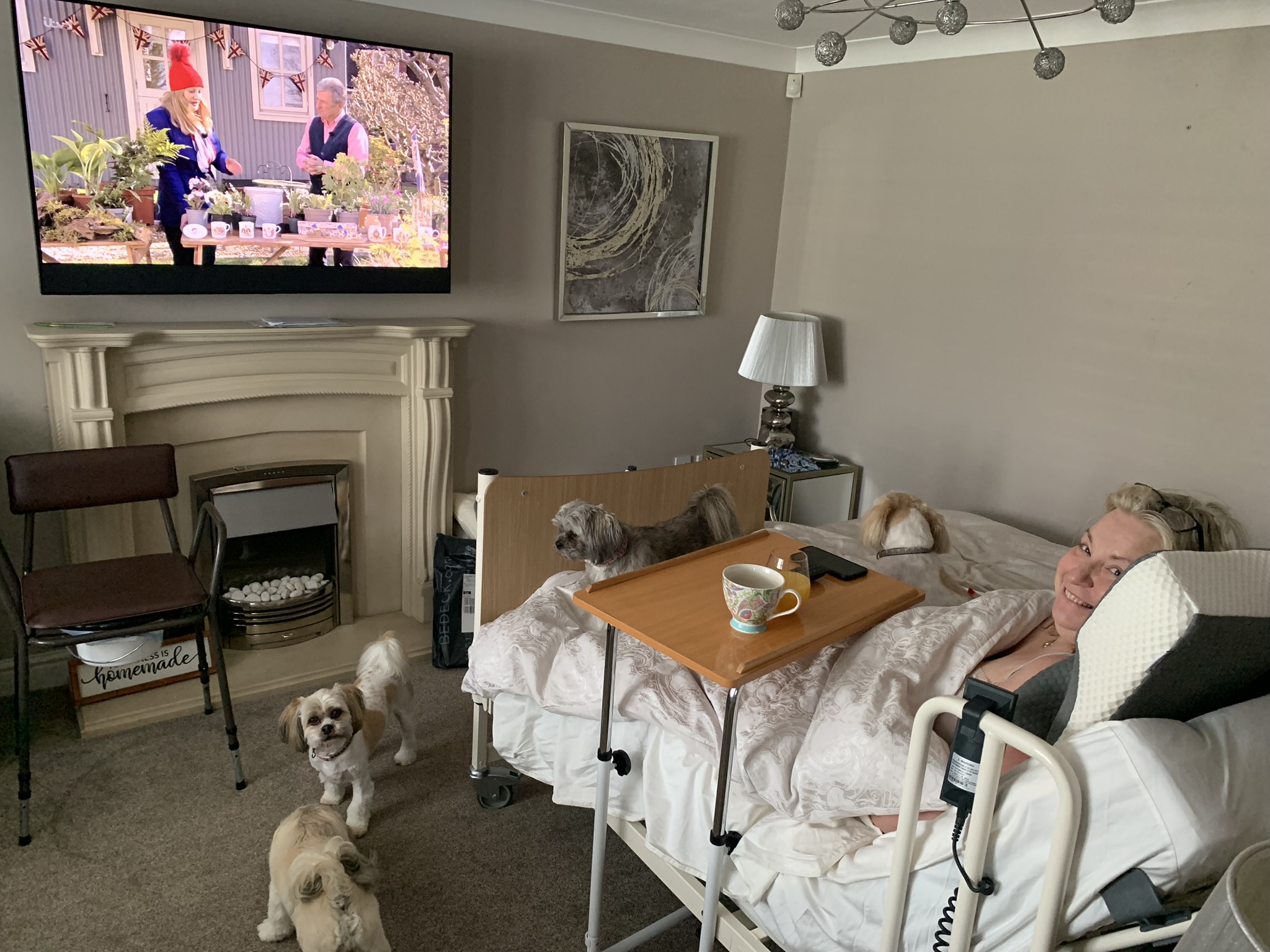 Julie at home in her hospital bed, she watches TV and smiles to the camera