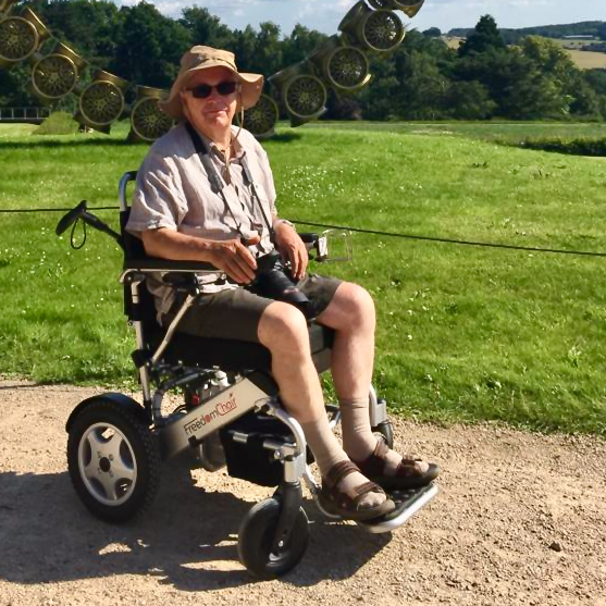 Mike in his wheelchair outside in front of a large sculpture and green field