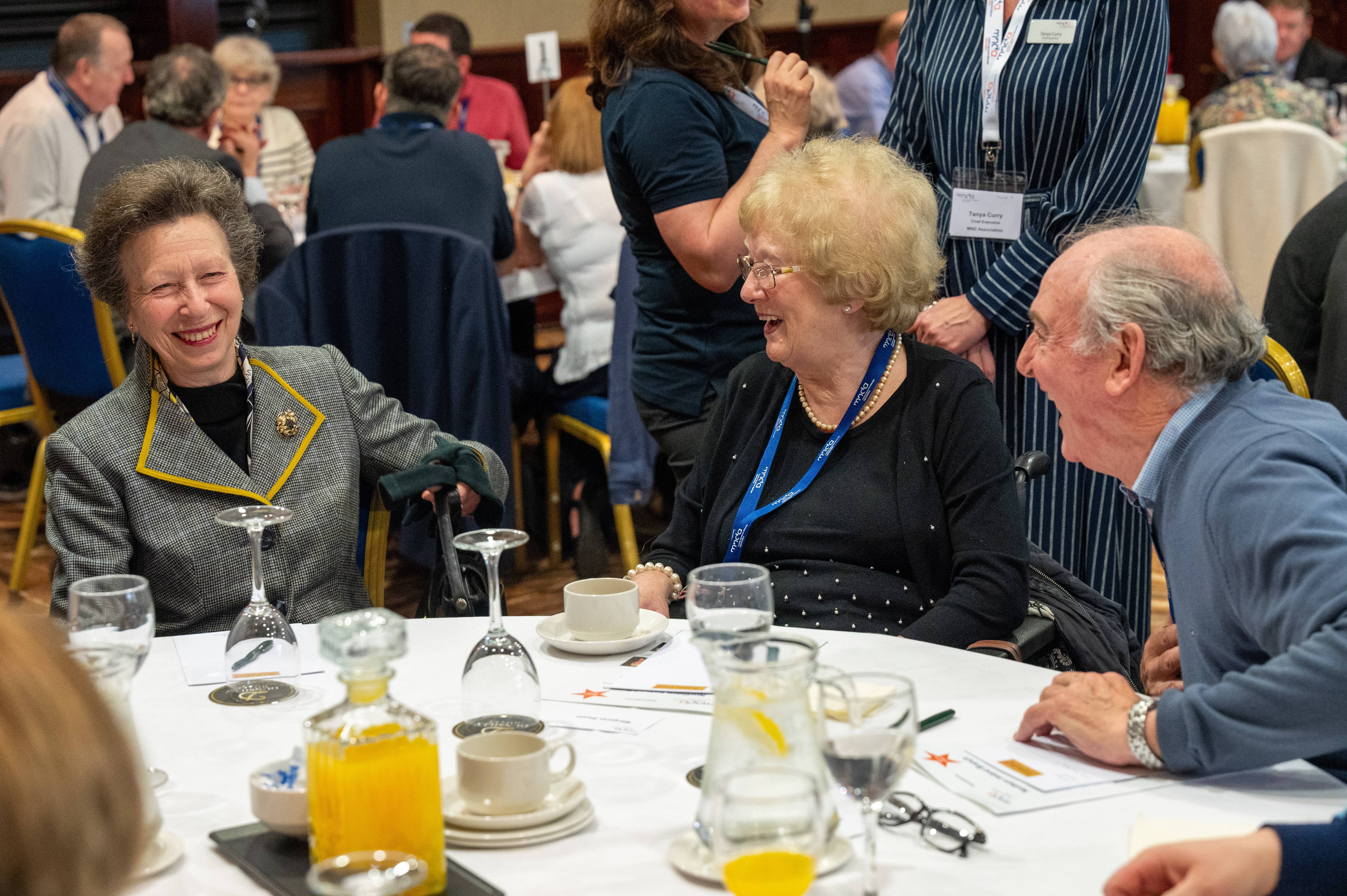 HRH The Princess Royal engaging in conversation and smiling at a table with a woman and man