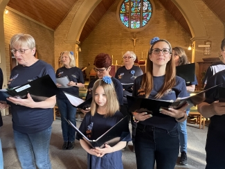 Action shot of 8 of the choir, singing, with music books in their hands.