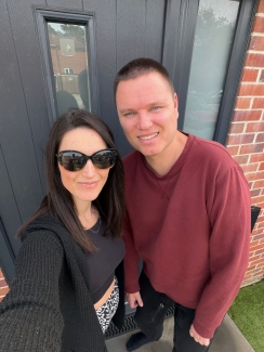 James and his wife Carly, stood outside their front door, smiling at camera.