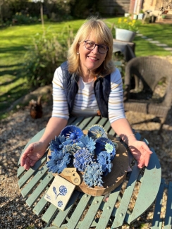 Linda sits in the garden showing the blue cornflowers made for fundraising