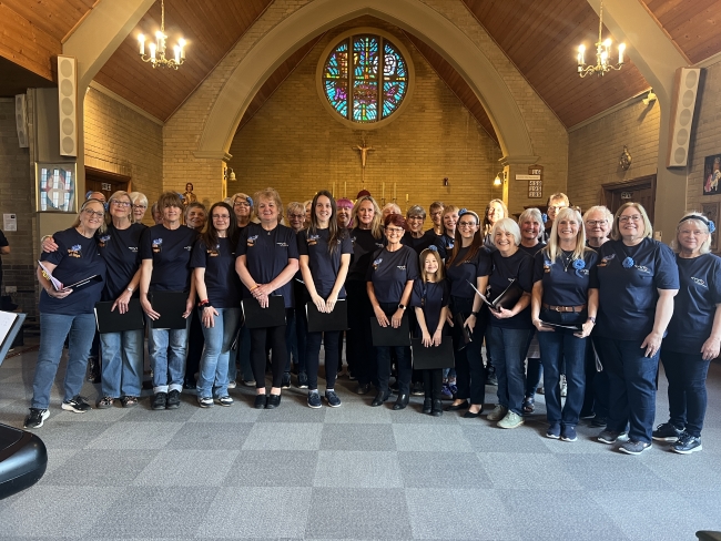 Photo of the choir in matching t-shirts, stood smiling at the camera