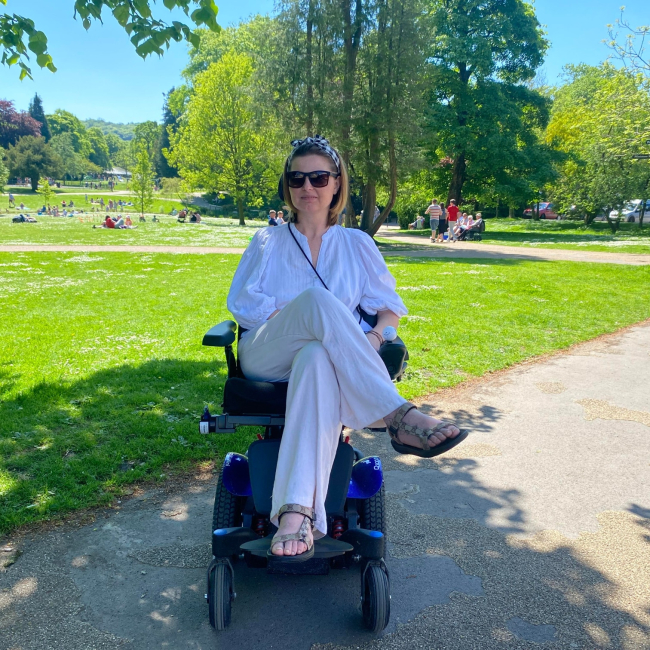 Kamila in her power chair smiling outside