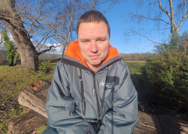 James looking directly at camera wearing a dry robe. He sits outside in nature.