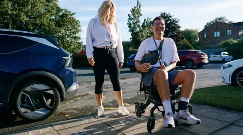 A man in wheelchair outside next to a woman standing. 