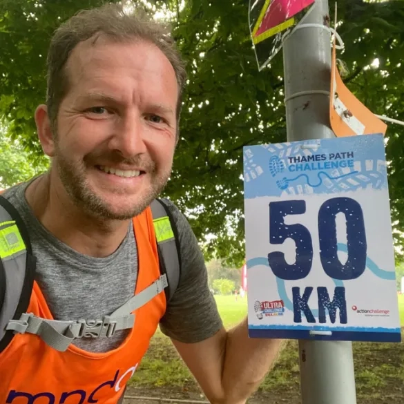 A man standing next to the 50km distance marker on the Thames path