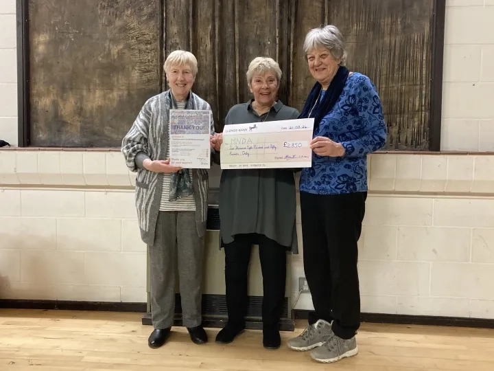 A group of MND Association volunteers standing holding a cheque. 
