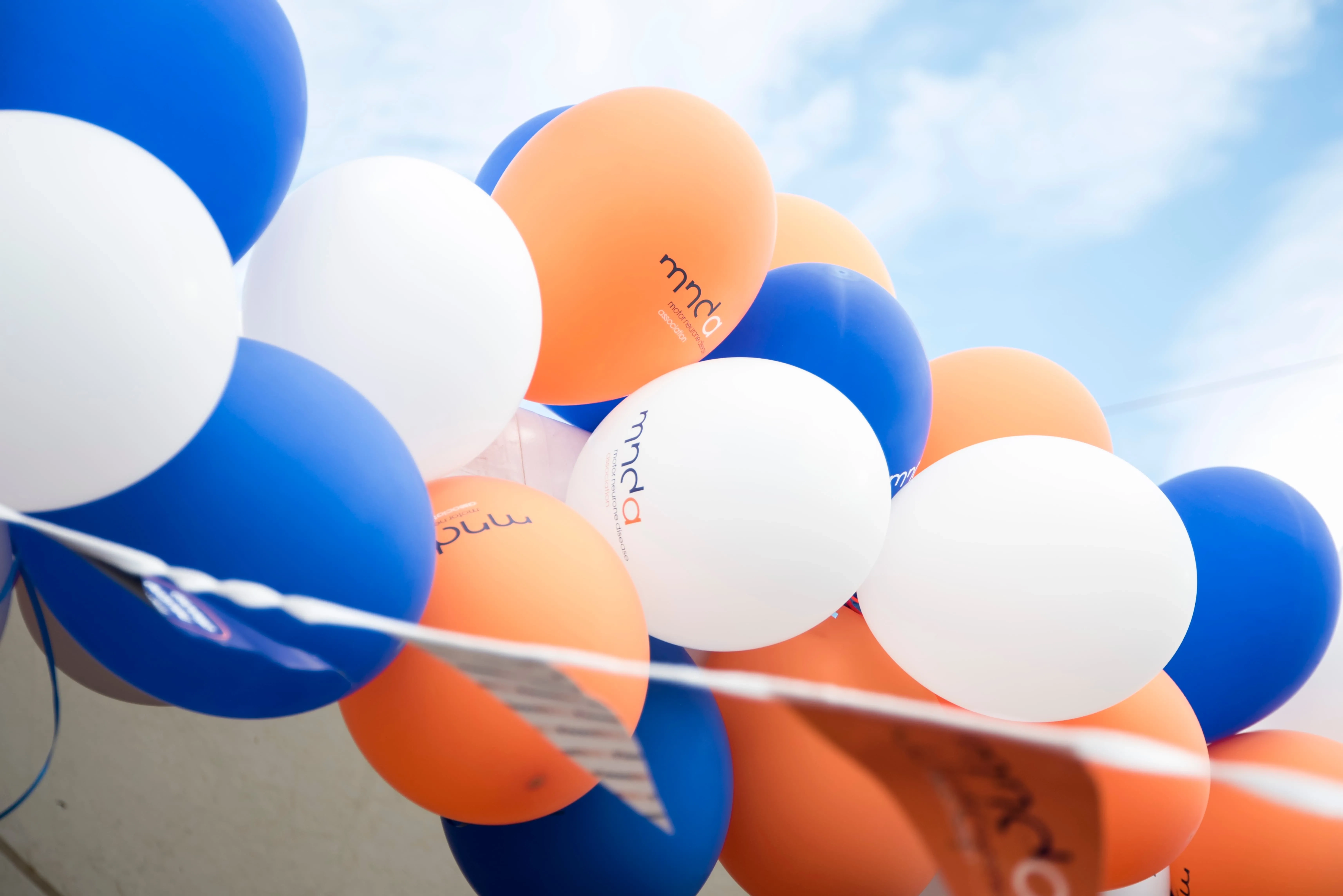 Orange, white and blue balloons in a row, printed with the MND Association logo.
