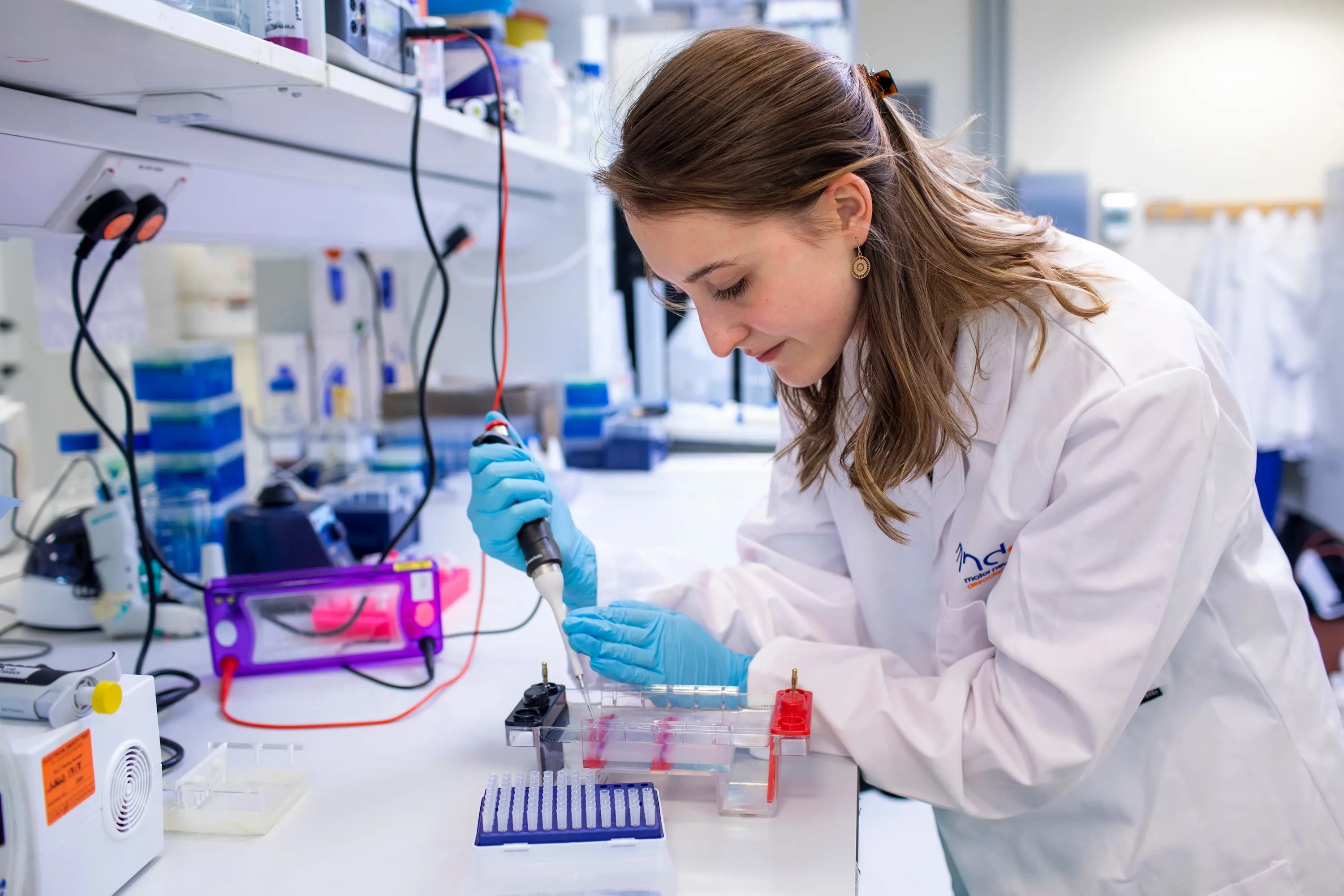 A researcher in a lab, wearing a white lab coat and using a pipette to transfer liquid.