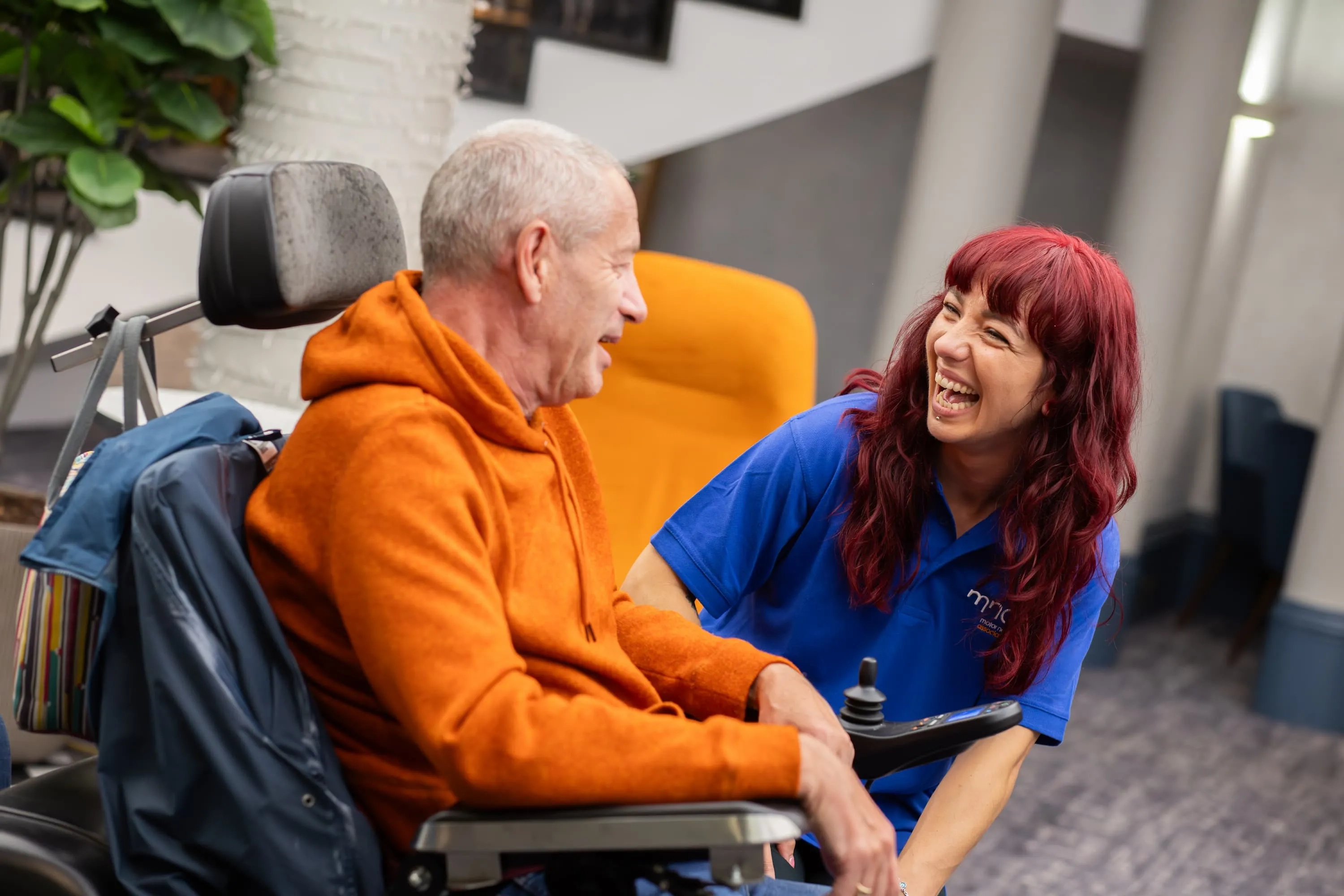 A person in a wheelchair in conversation with a member of MND Association event staff. They are laughing.