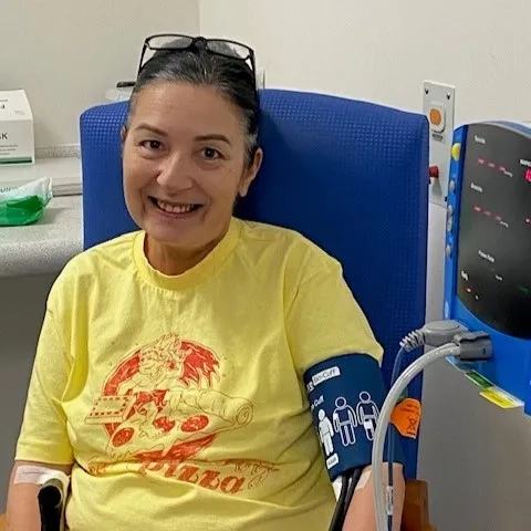 Debbie at a medical appointment. She is wearing a yellow tshirt and smiling at the camera.